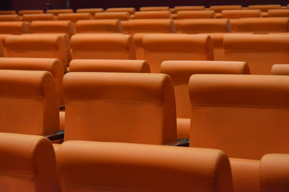 Multiple rows of green upholstered chairs with gold-colored metal frames arranged in an orderly fashion on a wooden floor. The chairs are clean and well-maintained, with a few chairs slightly overlapp